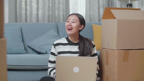 Asian Woman With Cardboard Boxes Comparing The House To Laptop After Moving Into A New House 