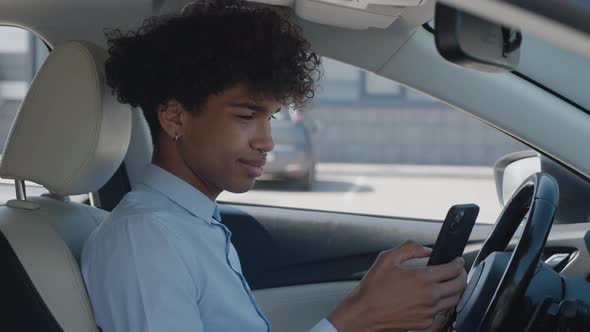 Handsome AfroAmerican Guy Sitting in Car to an Important Meeting and Typing on Her Cellphone