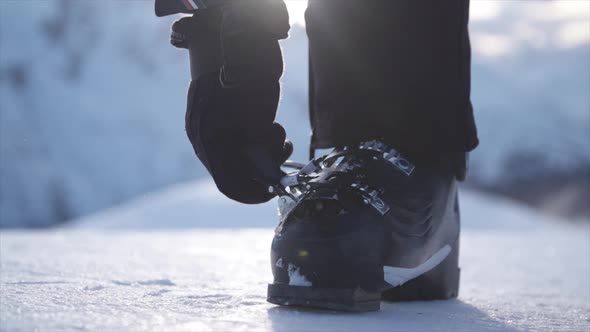 A woman with ski boots preparing to go skiing in the snow at a ski resort.