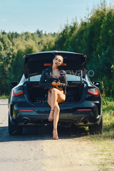woman in red lingerie and high heel shoes sits on the open trunk of a car