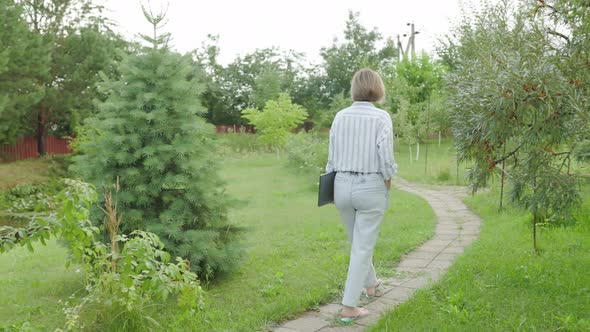 Carefree and easygoing woman walking at city park pathway or garden, carry notebook