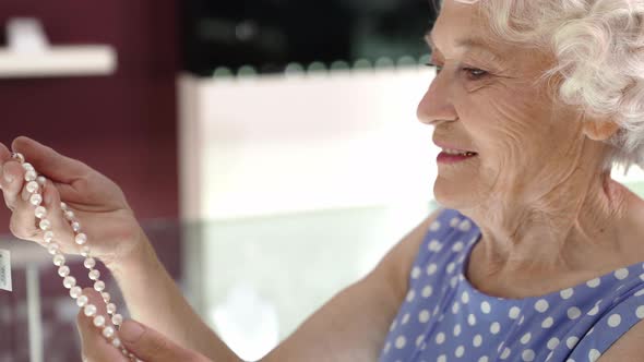 Side View of Elegant Aged Lady Buying Pearl Necklace at Shop