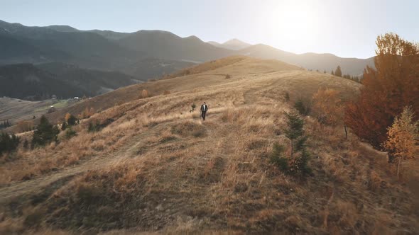 Aerial View Man Walks Up Mountain Road Sun Shines in His Back