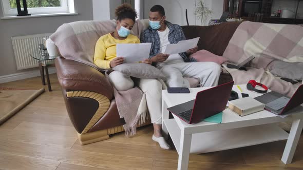 Wide Shot Portrait of African American Man and Woman in Coronavirus Face Masks Sitting on Couch