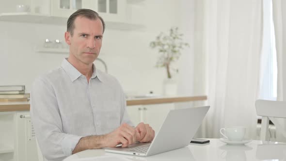 Serious Middle Aged Man with Laptop Looking at the Camera