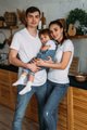 A happy young family spends time together in a home interior. Mom and dad kiss their baby - PhotoDune Item for Sale