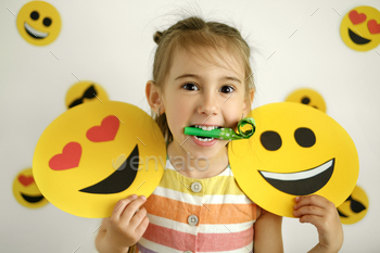  her mouth and an expression of happiness and surprise on her face holds a loving and happy emoticon in her hand