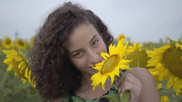 Portrait of Cute Curly Girl Jokingly Biting Big Sunflower in the Sunflower Field