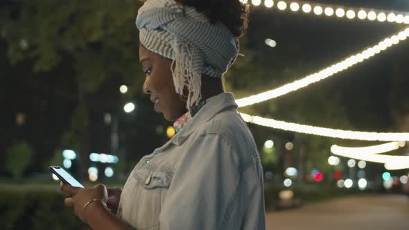 Afro Woman Messaging on Phone in Park in Evening