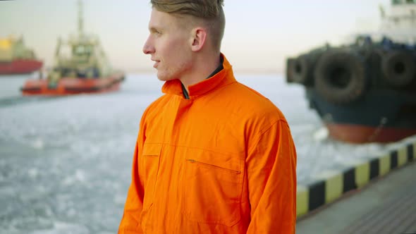 Dock Worker in Orange Uniform Looking at the Sea and Enjoying the Landscape of the Harbor in Winter