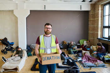 Male volunteer with donation box looking at camera against resting people