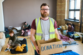 Bearded male volunteer with donation box looking at camera in refugee camp