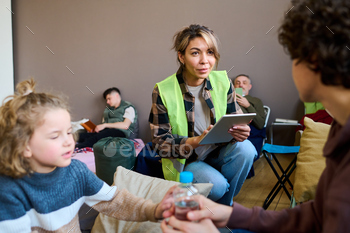 Young female volunteer with tablet sitting on squats in front of woman with son