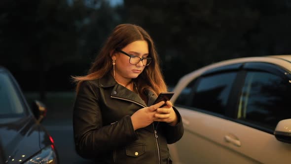 Woman Is Chatting in the Smartphone Against the Background of the Evening City