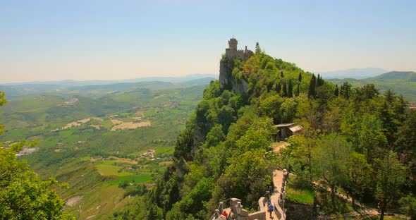 Towers On Top Of The San Marino Mountains With Tourist Trekking In Italy. Aerial Tilt-down Shot