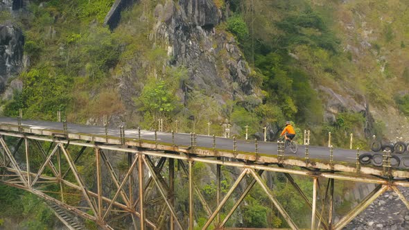 Drone View of Man on Bicycle Riding on Suspension Bridge in Mountains