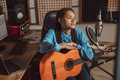 Young woman guitarist musician sitting in front of a microphone while recording new track - PhotoDune Item for Sale