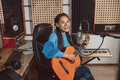 Woman singer playing guitar and singing new cool song into a microphone in music recording studio - PhotoDune Item for Sale