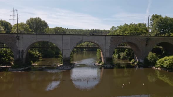 Person standing on the foot path of a  train trestle that leads over a green river in the countrysid