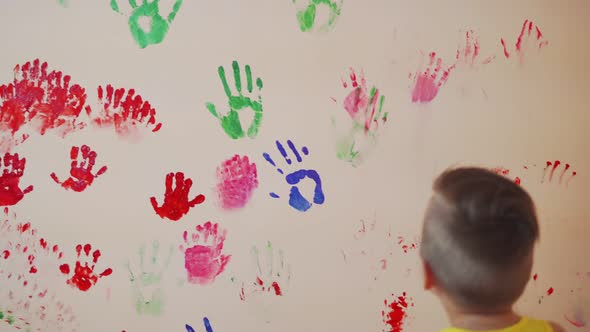 Happy Mother and Her Cute Boy Having Fun Together Leaving Their Colorful Handprints on the Wall