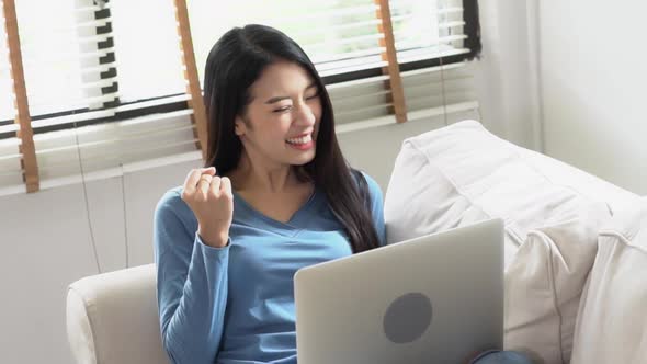 Young asian woman working online laptop with smile and happy sitting on couch at living room.