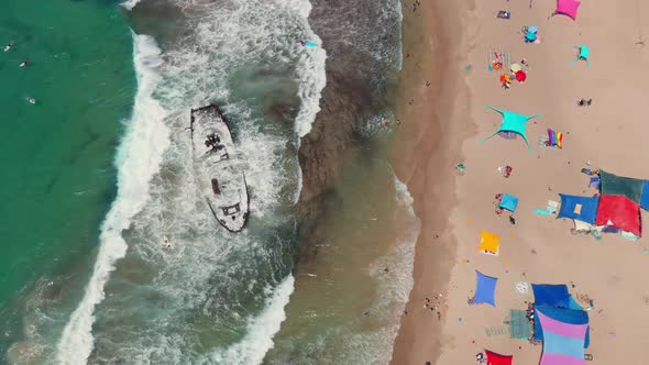 Picturesque summer beach with shipwreck and colourful umbrellas, aerial drone top down view 4k