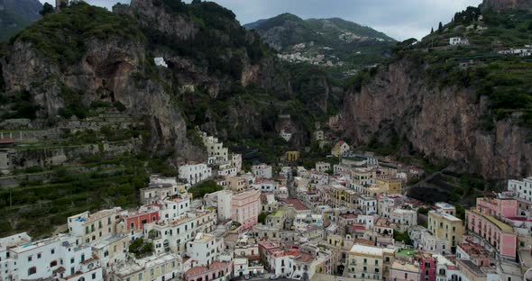Fly Over Dramatic Townscape Of Amalfi Behind Sheer Rocky Mountains In Campania, Italy. Aerial Drone