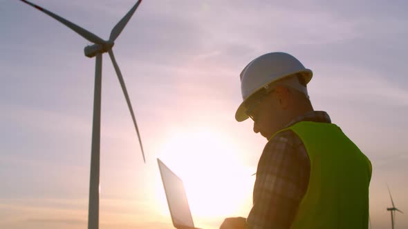 Windmill Engineer Watching Wind Turbines in Operation on a Laptop