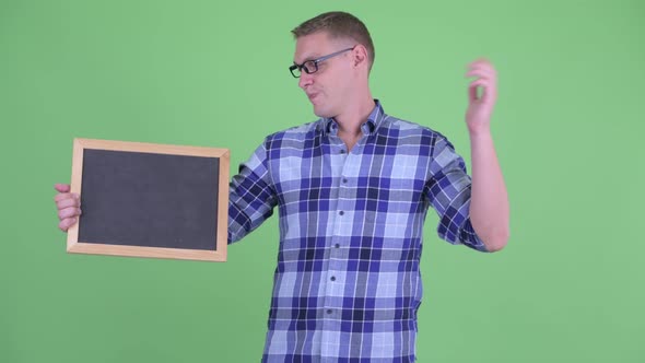Stressed Young Hipster Man Holding Blackboard and Giving Thumbs Down