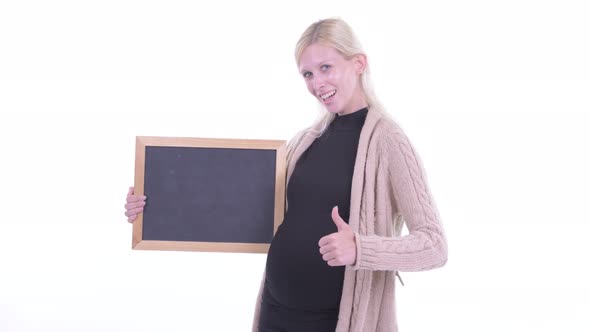 Happy Young Blonde Pregnant Woman Holding Blackboard and Giving Thumbs Up