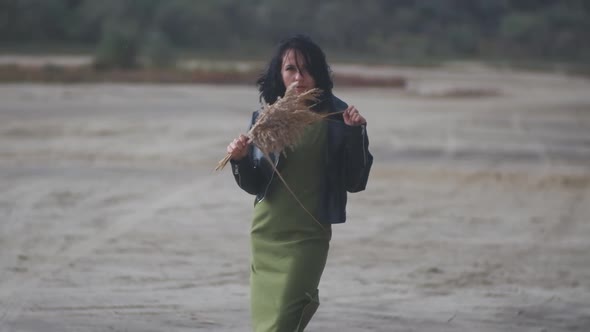 Beautiful Young Woman Walks in the Desert with a Bouquet of Flowers and Spikelets Under Rain