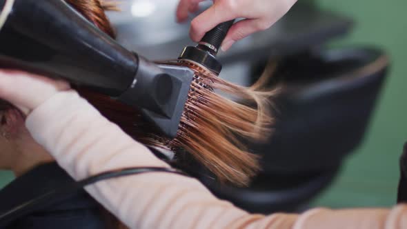 Female hairdresser blow drying hair of female customer at hair salon