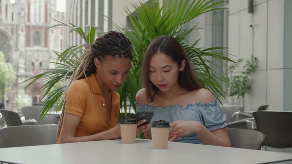 Two Young Girls Using Smart Phone at the Outdoors Cafe