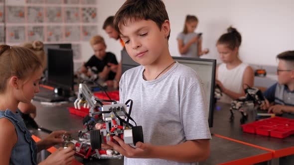 A Small Smart Boy Holds a Robot in His Hands in the Robotics Office