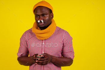 shirt with knitted scarf and hat feeling bad unwell with fever heat and chills in studio yellow background.flu and virus concept.