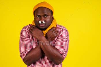 shirt with knitted scarf and hat feeling bad unwell with fever heat and chills in studio yellow background.flu and virus concept.