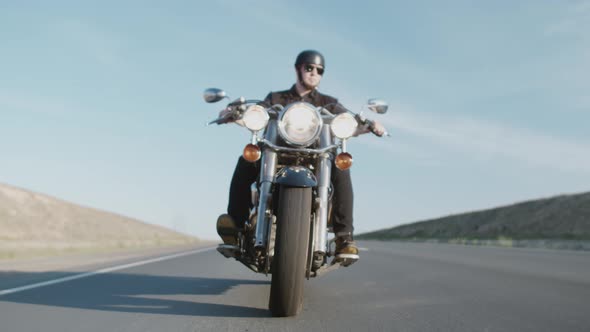 Biker in helmet and glasses on motorcycle rides on highway during day, goes to overtake, front view.