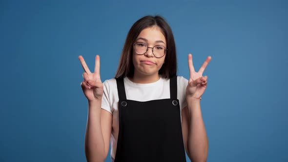 Asian Girl Showing with Hands and Two Fingers Like Quotes Gesture, Bend Fingers Isolated Over Blue