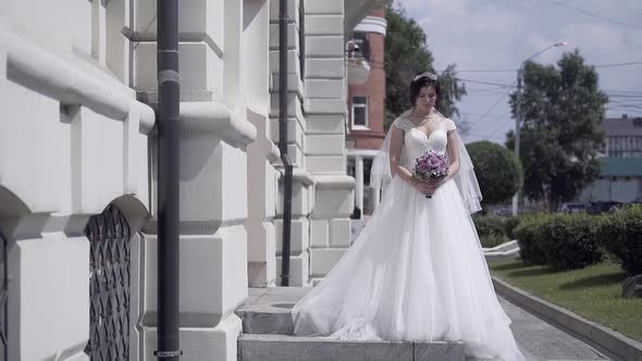 Slow Motion Bride in Wedding Dress Stands Near Building