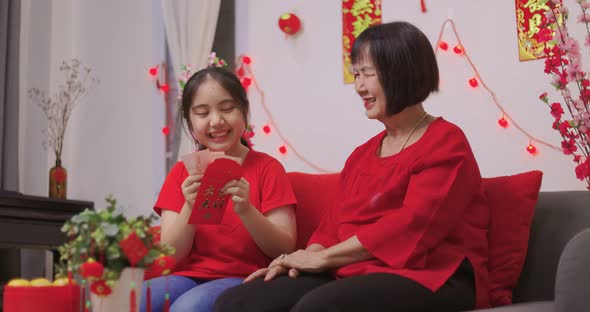 Happy Senior Asian Woman Giving Her Granddaughter A Lucky Red Envelope for Chinese New Year Gift.