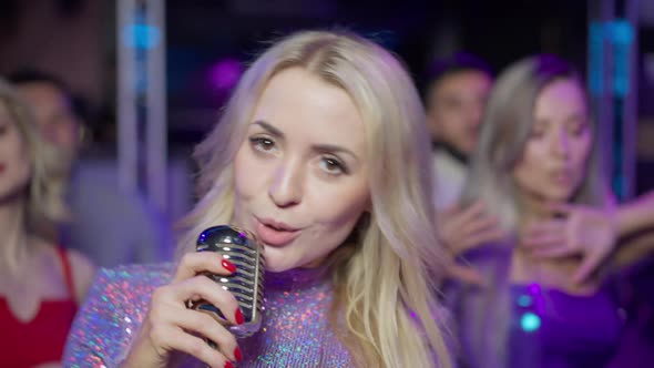 Slim Blond Beautiful Woman with Brown Eyes Singing with Microphone Looking at Camera As Fans