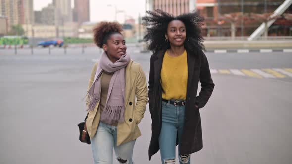 Two smiling young women walk along the city street