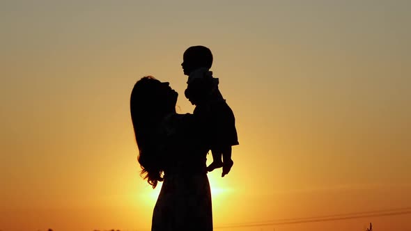 Unrecognizable Silhouette at Sunset Happy Mother Throws Up Her Baby