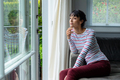 Thoughtful caucasian young woman looking through window while sitting at home - PhotoDune Item for Sale