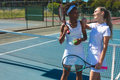 Smiling multiracial female tennis players talking while taking break at court on sunny day - PhotoDune Item for Sale