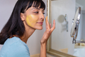 Caucasian young woman looking at mirror and applying facial mask in bathroom - PhotoDune Item for Sale