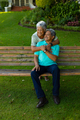 Biracial smiling senior woman embracing senior husband sitting on bench and looking away in park - PhotoDune Item for Sale