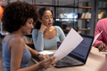 Biracial businesswomen discussing over laptop and document together during meeting at workplace - PhotoDune Item for Sale
