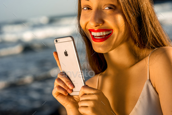 nd happy woman holding new iPhone 6s Space Gray on the blurred sea background. iPhone 6 was created and developed by the Apple inc.
