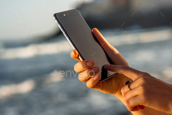 hands holding new iPhone 6s Space Gray on the blurred sea background. iPhone 6 was created and developed by the Apple inc.
